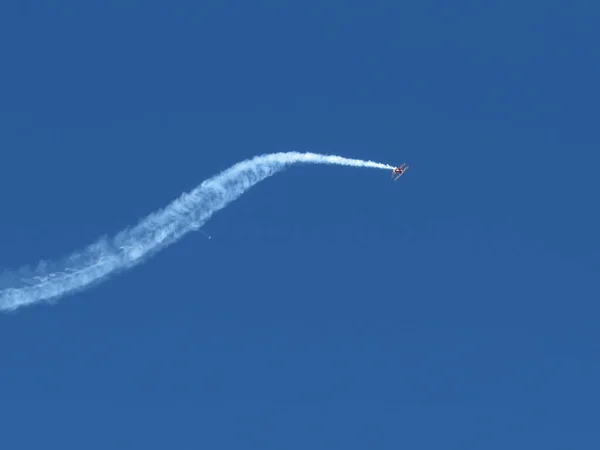 Маленький акробатический самолет и след в голубом небе — стоковое фото