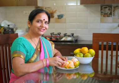 Kahvaltı masasında portakallı gülümseyen kadın, portakal yiyen Hintli kadın. Sağlıklı beslenme rızası.                               