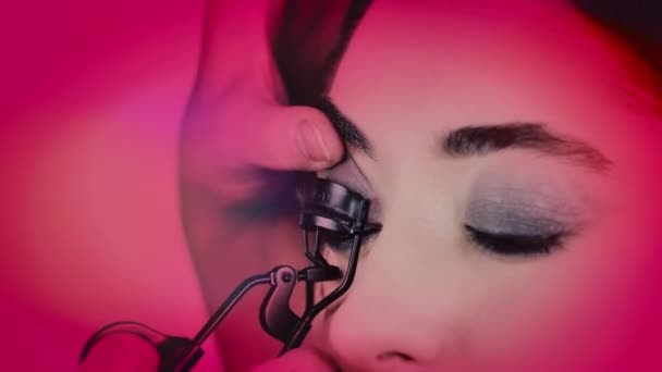 Elegante primer plano tiro de un artista de maquillaje usando rizador en las niñas jóvenes pestañas — Vídeos de Stock