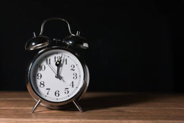 Antika çalar saat mahsulü, ahşap bir masa üzerinde çan metaliği ve gece yarısı siyah arka plan yakın plan.