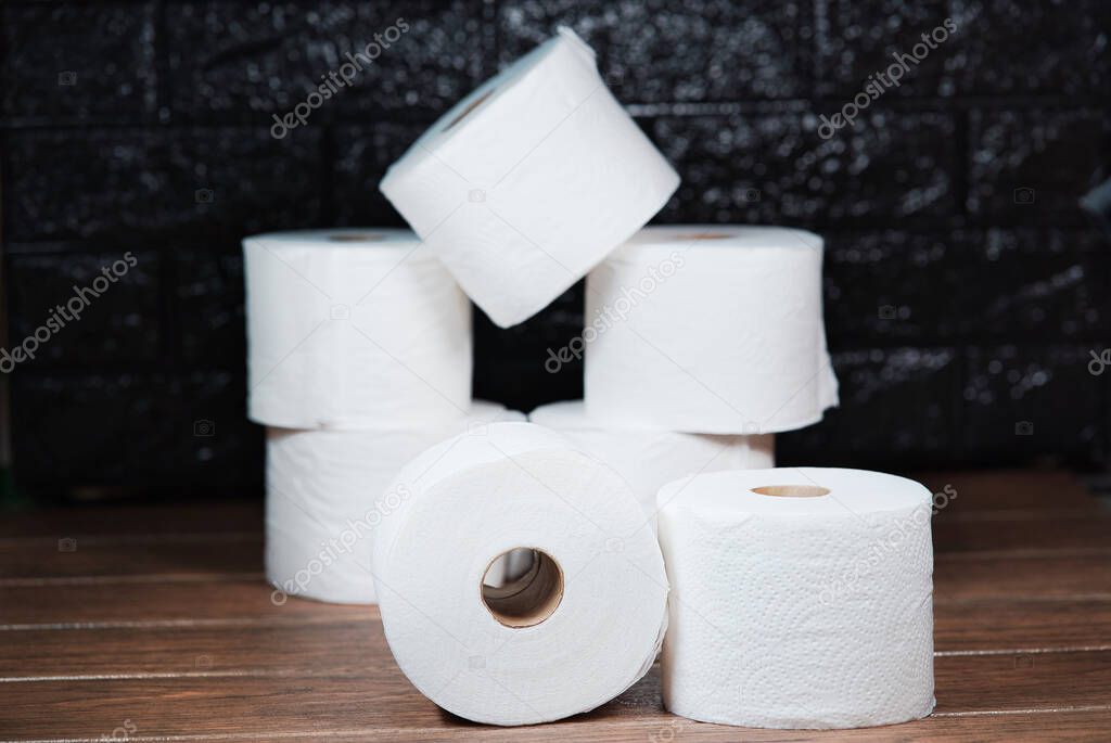 Rolls of white disposable bathroom toilet paper on a brown wooden table and dark background