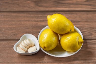 Tahta bir masada düz tabakta C vitamini tabletli dört taze sarı limon.