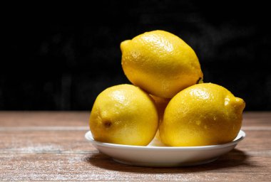 Ahşap bir masada tabakta taze sarı limon ve koyu seramik zemin