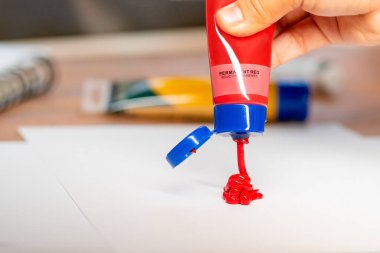 Kağıt üzerine kırmızı akrilik boya ve arka planda sarı akrilik boya bırakıyor.