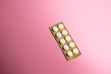 Pembe arka planda 10 haplık beyaz bir hap paketi.