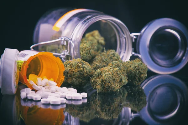 Cannabis buds and prescriptions pills over reflective surface - — Stock Photo, Image