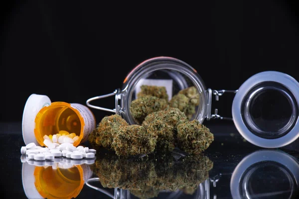 Cannabis buds and prescriptions pills over reflective surface - — Stock Photo, Image