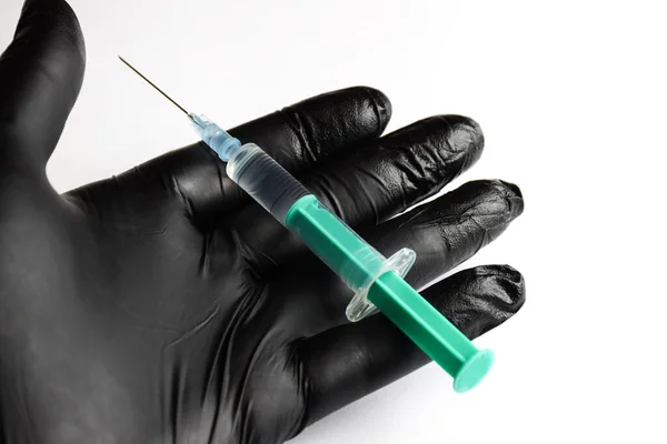 白い背景にプラスチック製の注射器と針が付いている黒い手袋で手 — ストック写真