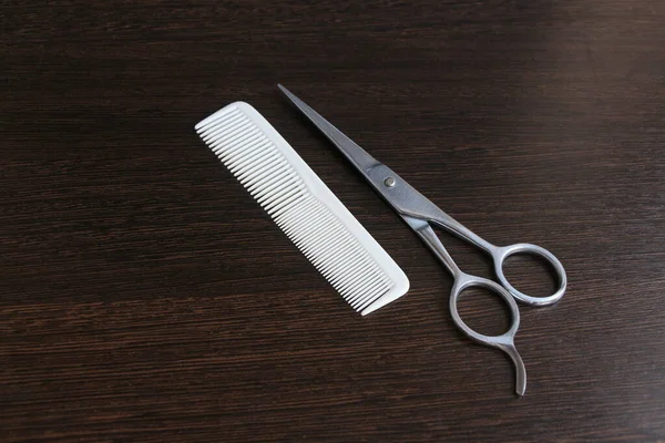 Hairdressing scissors and white comb lies on the wooden table. Haircut tools theme.