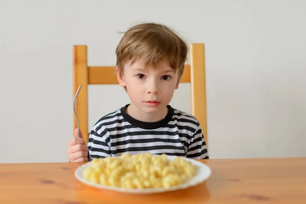 A boy sits at a table with a pasta dish