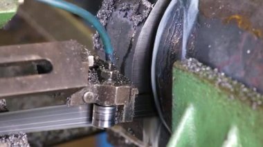 Yüksek hızda dişleri olan metal bir bant, yuvarlak, sağlam bir metal işçiliğini testereyle silindirlerden geçirir. Soğutucu su yukarıdan akar. Yakın plan..