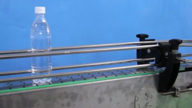 Bir adamın eli, taşıma bandına karbonatlı su dolu plastik şişeler koyar. Şişeler kemerin üzerinde hareket ediyor.