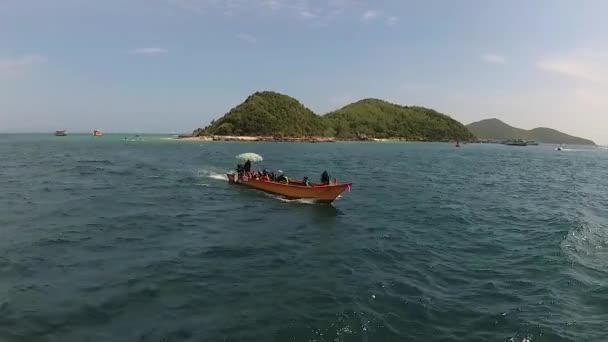 海では カメラ付きの船が乗客と大きな木製のボートの前を航海します 遠くには大きな島が見えます — ストック動画