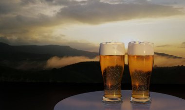 Üç boyutlu cam bira ve dağ manzaralı arka plan. Tepenin tepesinde gün batımı ve sis var..