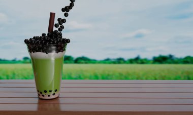 Bubble milk green tea in  a clear glass and brown straws placed on a wooden table and blur the background of the rice field. 3D rendering  clipart