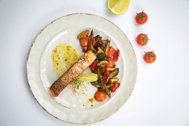 Sebzeli ızgara somon, beyaz tabakta limon.