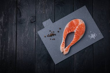 Gri tahtada çiğ somon bifteği ve siyah arka plan