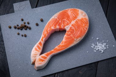 Gri tahtada çiğ somon bifteği ve siyah arka plan