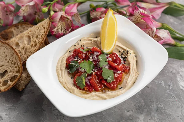 Gri arka planda bir dilim limon olan humus.