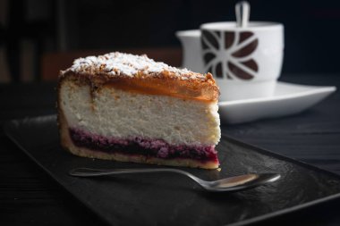 Siyah tabakta peynirli kek ve siyah bir arka planda kaşık.