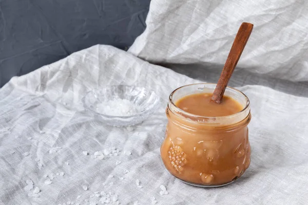 Gri tekstil arka planında ev yapımı tuzlu karamel soslu cam kavanoz..