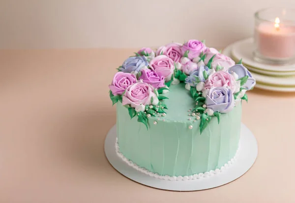 Düğün için turkuaz bir pasta ve krema gülleri. Pembe arka planda. Beyaz tabaklarda pembe bir mumla