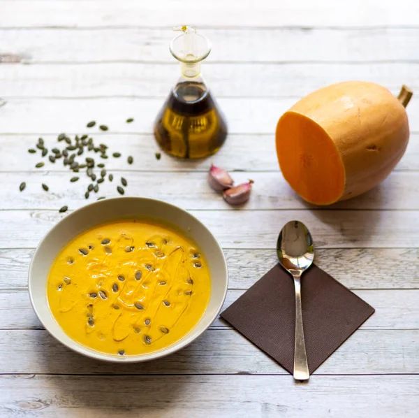 Balkabağı kreması beyaz ahşap masa üzerinde balkabağı çekirdeği ve zeytinyağı