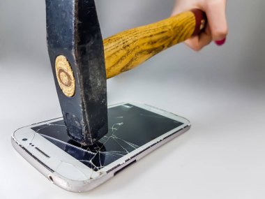 Beyaz bir yüzey üzerinde dinlenen akıllı telefona çarpan bir çekiç ekranı paramparça eder..