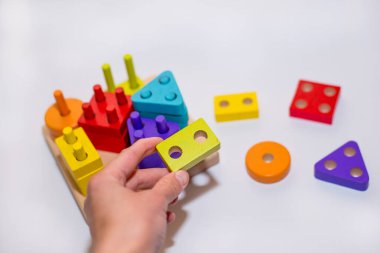 Beyaz arka planda tahtadan yapılmış çocuk oyuncağı, çocuk tasarımcıyla oynuyor, sıralayıcı. Oyuncak dolu çocuk odası. Bir çocuğun ellerinde inşaatçı. Arka planda ahşap evler. Karantinaya alınmış evde eğitim.