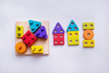 Beyaz arka planda tahtadan yapılmış çocuk oyuncağı, çocuk tasarımcıyla oynuyor, sıralayıcı. Oyuncak dolu çocuk odası. Bir çocuğun ellerinde inşaatçı. Arka planda ahşap evler. Karantinaya alınmış evde eğitim.