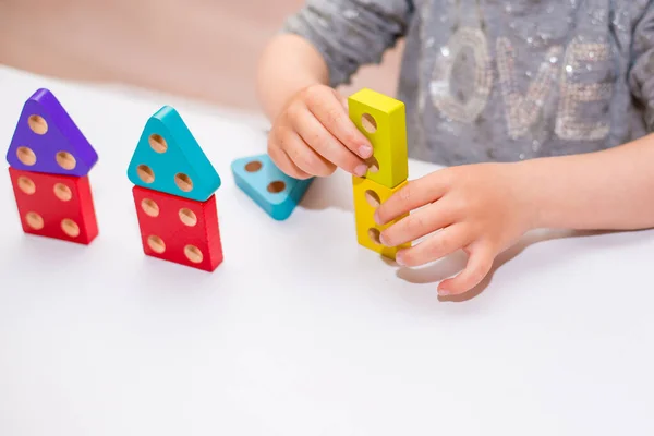 Children\'s toy made of wood on a white background close-up, the child plays with the designer, sorter. Children\'s room with toys. Constructor in the hands of a child. Wooden houses in the background . Quarantined home schooling.