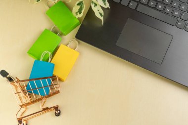 İnternet alışveriş konsepti. Küçük alışveriş arabası, kutular, renkli çantalar, banka kartı, dolarlar dizüstü bilgisayarda duruyor.