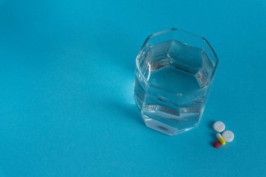 Mavi arka planda birkaç hap olan bir bardak su.