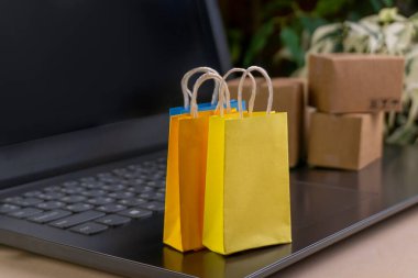 İnternet alışveriş konsepti. Küçük alışveriş arabası, kutular, renkli çantalar, banka kartı, dolarlar dizüstü bilgisayarda duruyor.