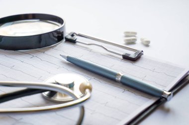 Masada steteskop, kalem, büyüteç, hap ve gözlüklü kardiyogram duruyordu.