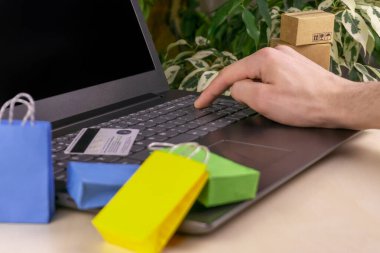 İnternet alışveriş konsepti. Küçük alışveriş arabası, kutular, renkli çantalar, banka kartı, dolarlar dizüstü bilgisayarda duruyor.