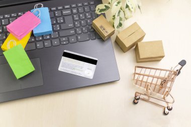 İnternet alışveriş konsepti. Küçük alışveriş arabası, kutular, renkli çantalar, banka kartı, dolarlar dizüstü bilgisayarda duruyor.