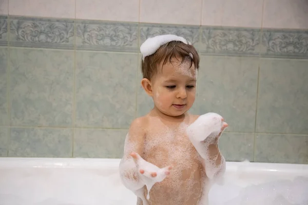Милий хлопчик приймає ванну, дивлячись на мильну піну в руках. крупним планом, м'який фокус, фон ванна кімната в розмитому — стокове фото