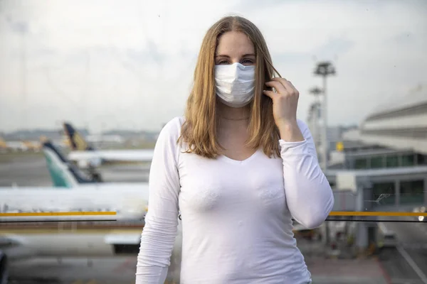 Retrato de una hermosa chica caucásica en una máscara médica respiratoria mirando a la cámara. en los aviones de fondo y el aeropuerto en desenfoque. concepto epidémico de coronavirus, covid-19 . — Foto de Stock