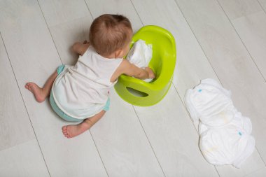 Lazımlığı kullanmayı öğrenme konsepti. Yakın plan: küçük şirin bir bebek yerde oturur ve oynar: yeşil bir gece çanağına temiz bebek bezi koyar. Yakın çekim, üst görünüm