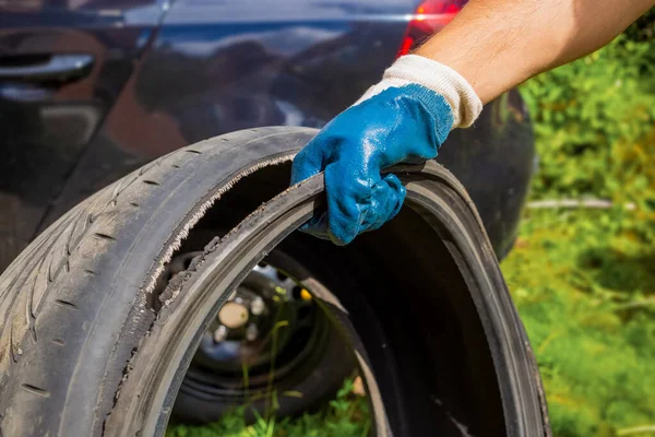 the hand of the master in a blue glove holds the torn tire. tire repair, tire repair. in the background black car in blur
