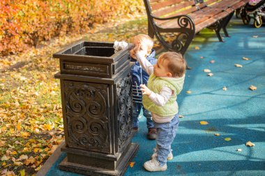 Parktaki siyah konteynırın yanında duran iki küçük şirin bebek ve oraya çöp atıyorlar. Arkadan başka bir çocuk geliyor. yumuşak odak, bulanık arkaplan.