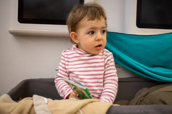 Pequeño bebé lindo despertó en el capazo del bebé de un avión sentado soñoliento mirando alrededor, primer plano, enfoque suave — Foto de Stock