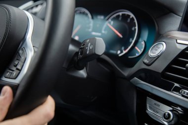 Modern bir arabanın direksiyonunun altındaki stop düğmesini kapat. Erkek eli direksiyonu tutar, yol gösterir. Arkaplanda bulanık hız göstergesi