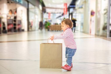 Kara Cuma konsepti, çocuklarla alışveriş, doğa dostu alışveriş. Küçük şirin kız alışveriş için büyük bir kağıt torba yakalıyor. yakın plan, yumuşak odak, arka plan dükkanları, yan görünüm