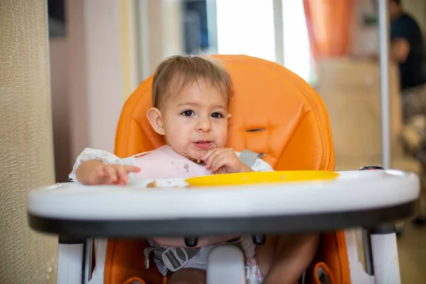 귀여운 아기는 얼굴에 부스러기가 오렌지 의자에 위에는 부스러기와 오렌지 플라스틱 — 스톡 사진