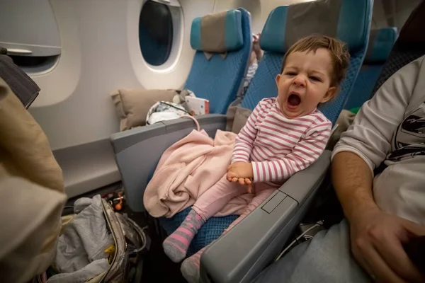 Liten söt sömnig småbarn sitter i ett flygplan säte och gäspar tröttsamt — Stockfoto