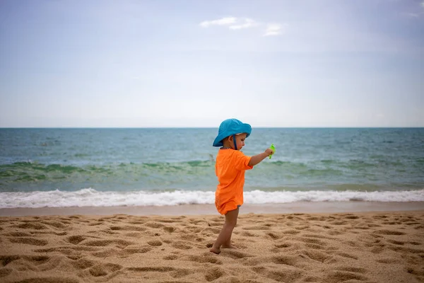 青い帽子の赤ちゃんビーチを歩く。サイドビュー。隔離、移動の自由、国境の開放 — ストック写真