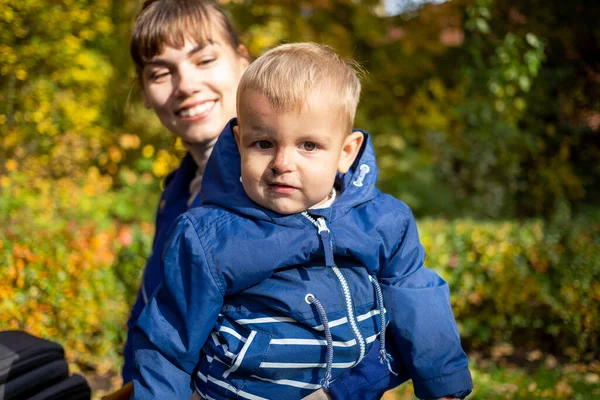 Bayi laki-laki Kaukasia kecil yang lucu dengan wajah kotor duduk dalam pelukan ibu. Wanita berbaju biru melihat anaknya dan tersenyum. close-up, soft focus. di hutan latar atau taman — Stok Foto