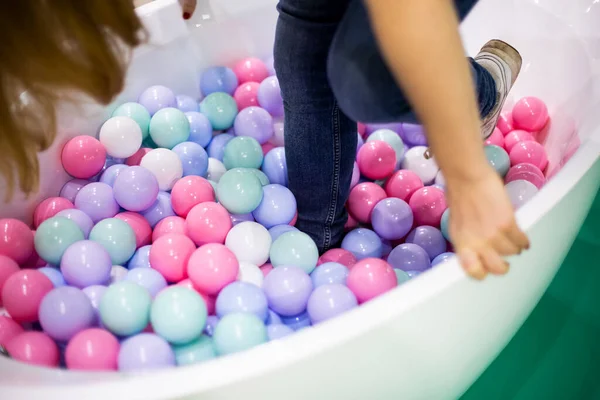 Menina com cabelo loiro longo em jeans azul invade a piscina com bolas de plástico de cores pastel rosa, branco, roxo, verde, hortelã. close up, foco suave . — Fotografia de Stock